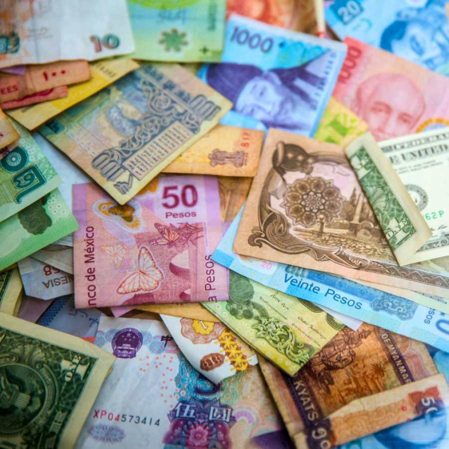 A pile of various international banknotes including US dollars, Mexican pesos, and others, with some denominations visible such as 50 pesos and one dollar.