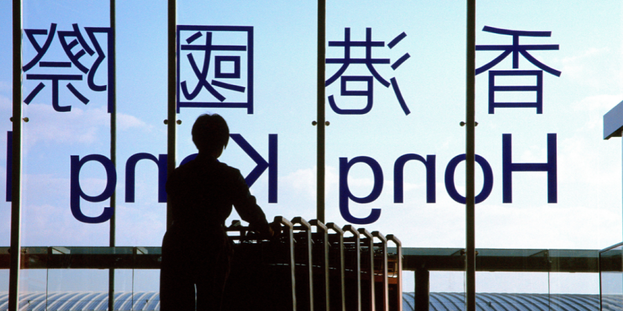 Silhouette of a person standing at a railing in front of a glass wall with large Japanese characters visible through the glass window panels.
