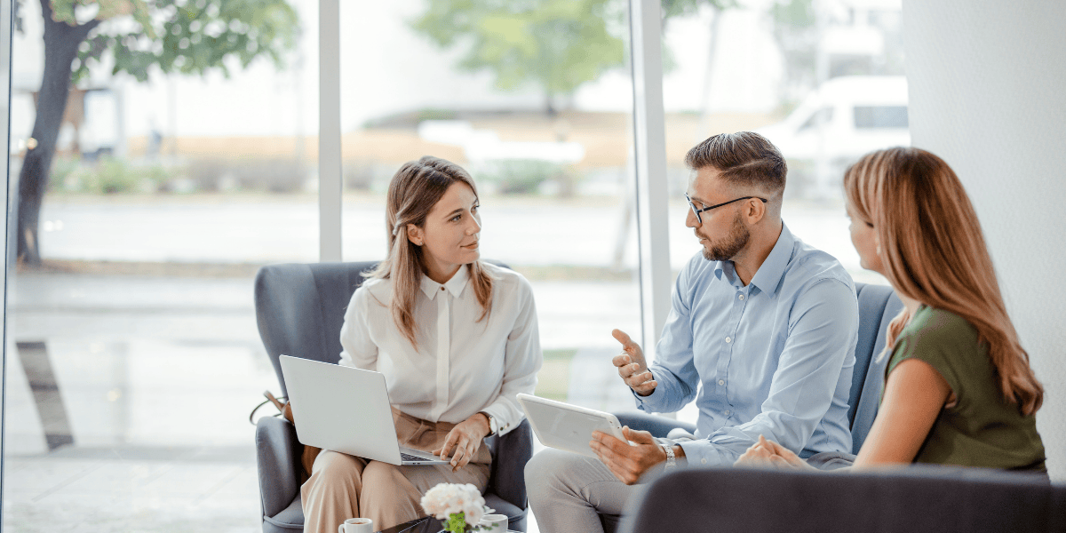 woman holding laptop in business meeting with two other people in an open office