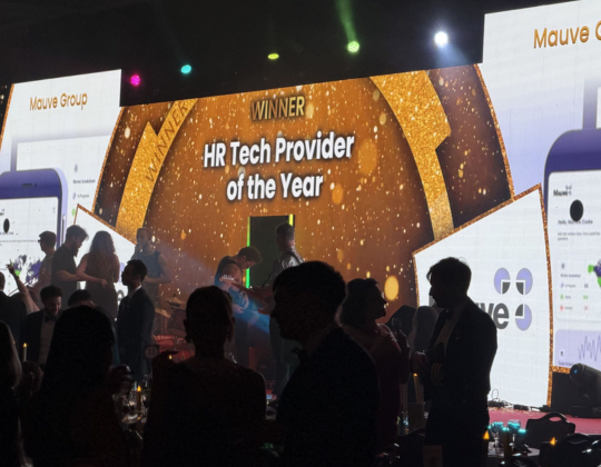 The Mauve Group is awarded HR Tech Provider of the Year, displayed on a large screen with sparkling golden accents and images of their mobile app.
