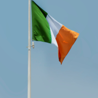 The flag of Ireland, green, white, and orange, waves against a clear blue sky on a flagpole.