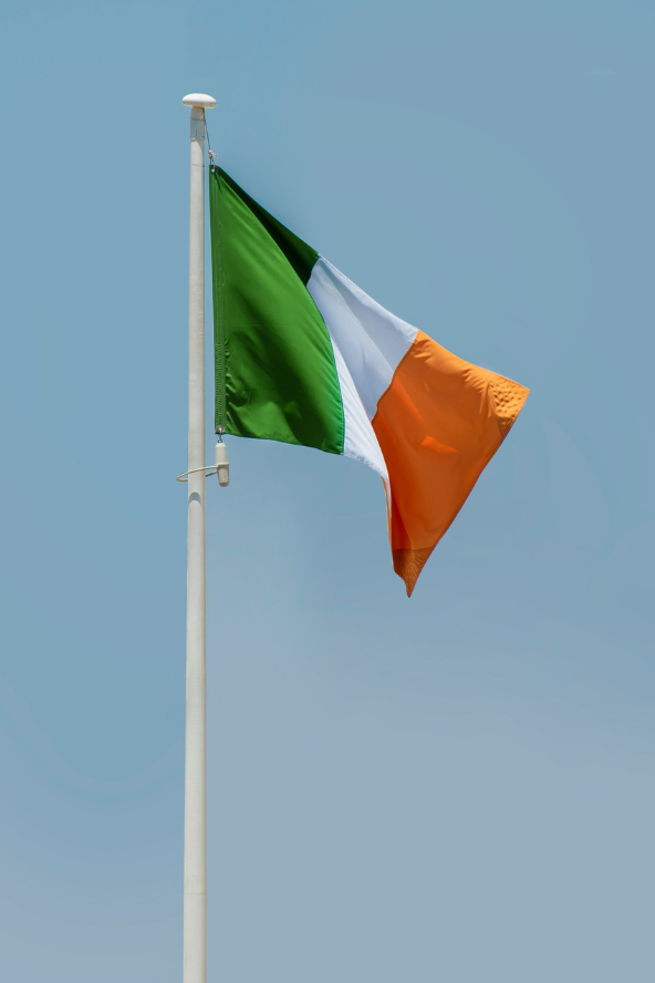 The flag of Ireland, green, white, and orange, waves against a clear blue sky on a flagpole.