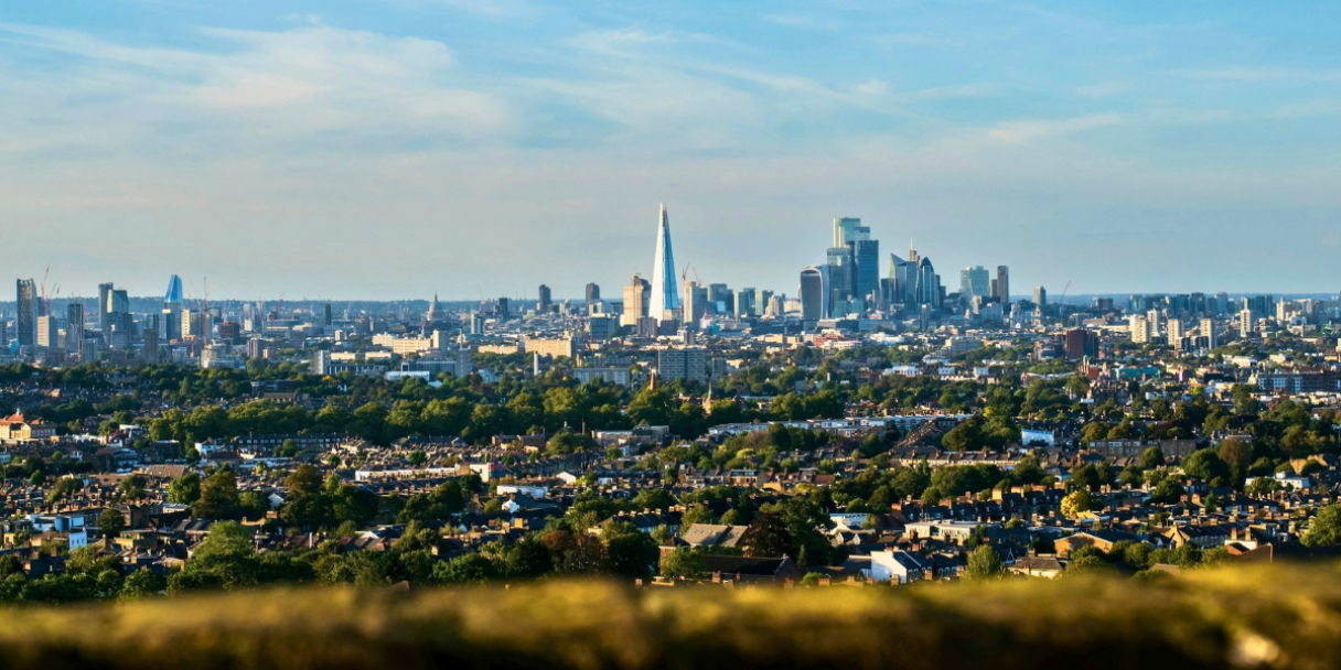 Wide skyline view of a London under a blue sky, with dense neighbourhoods in the foreground and tall skyscrapers in the distance.