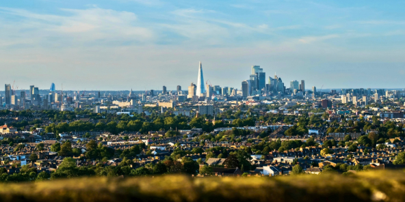 Wide skyline view of a London under a blue sky, with dense neighbourhoods in the foreground and tall skyscrapers in the distance.