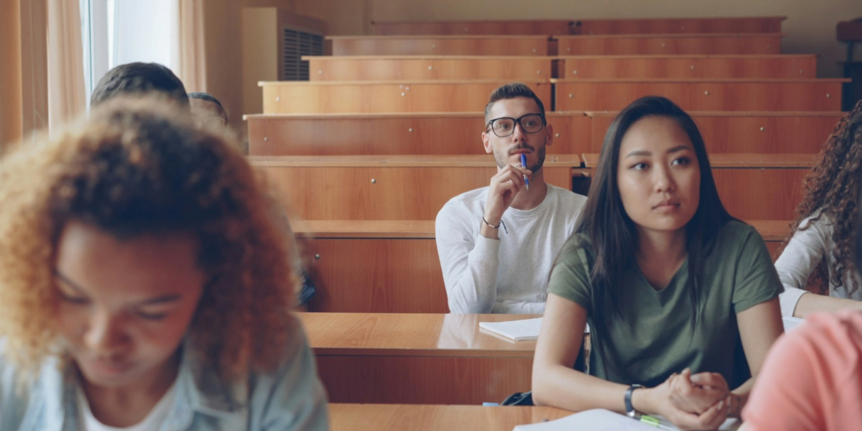 A group of university students are sat in a lecture hall attending a class.