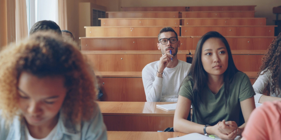 A group of university students are sat in a lecture hall attending a class.