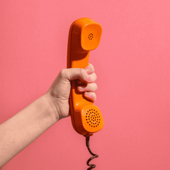 a person holding an orange telephone on a pink background