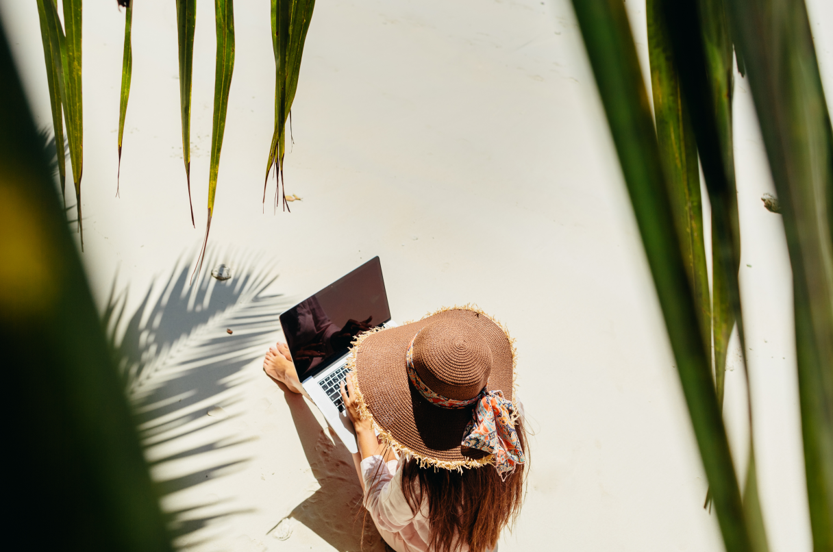 Un trabajador nómada digital en una playa, con sombrero para el sol