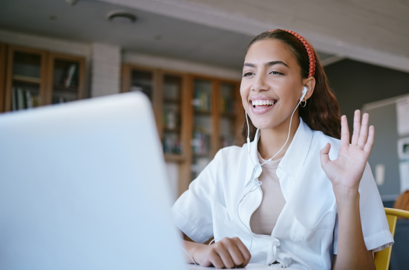 Mujer sudamericana sonriendo y saludando a la pantalla de un portátil mientras participa en un seminario web.