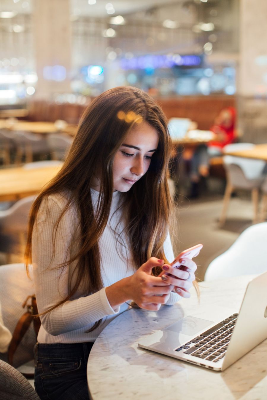 Chica con teléfono y portátil en una cafetería